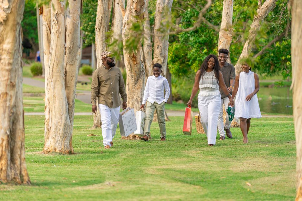 Group walking through a tree-lined path in coordinated casual outfits carrying picnic supplies.
