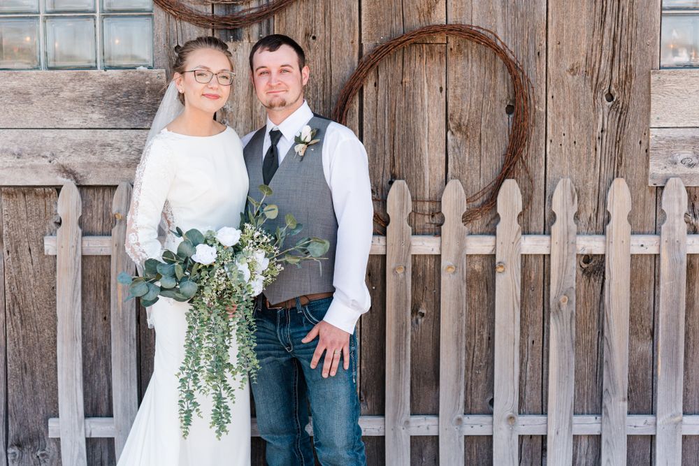 A wedding portrait showcasing casual country attire against rustic wooden barn backdrop.