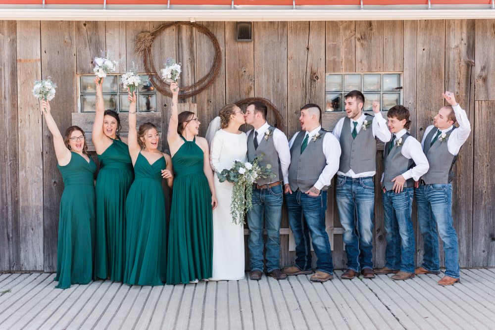Wedding party celebrates with raised arms wearing emerald dresses and casual gray vests.