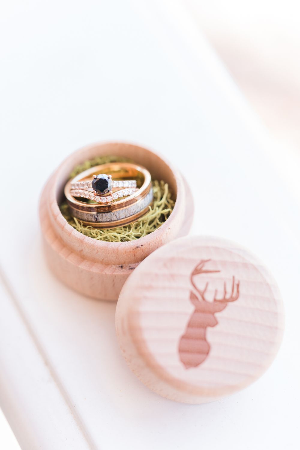 Wedding rings nestled in a pink wooden box with a deer silhouette design on the lid.