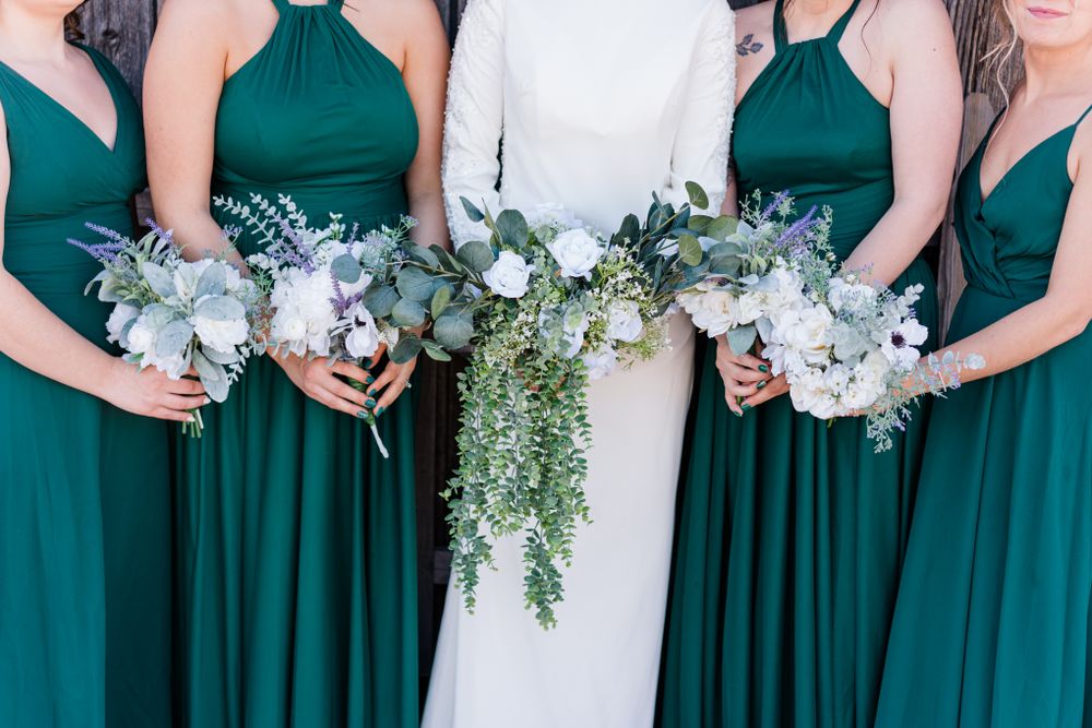 Wedding bouquets with cascading greenery and white flowers held against emerald green dresses.