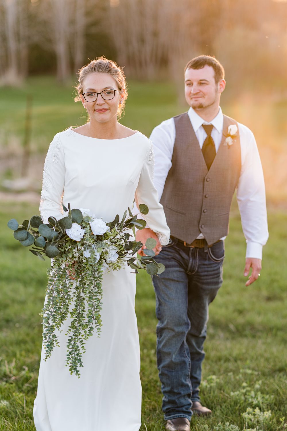 Bride holds cascading eucalyptus bouquet while standing with groom in outdoor setting.