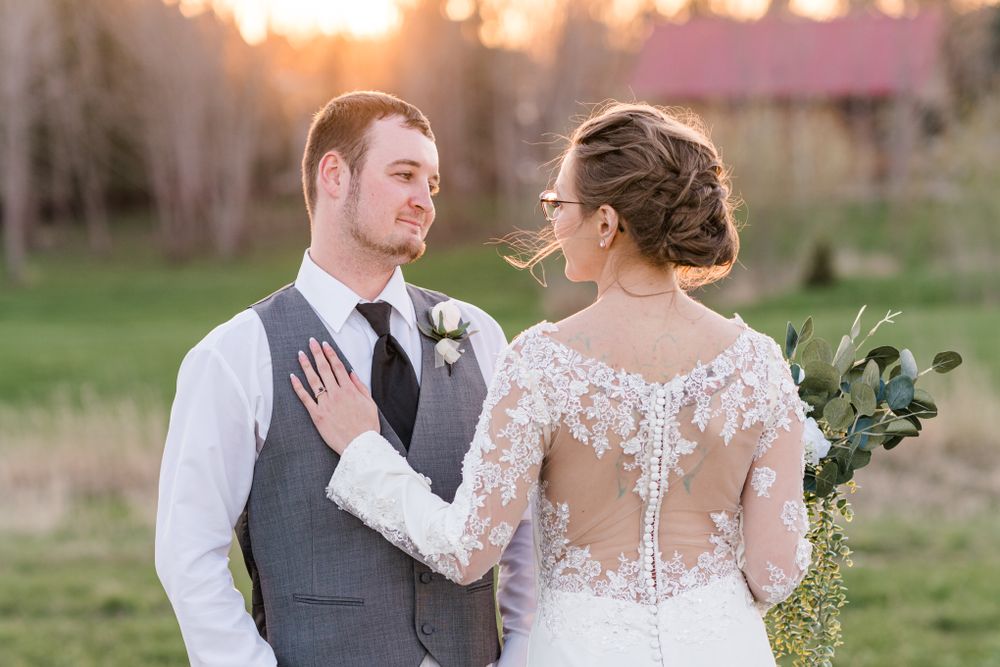 A romantic sunset wedding photo shows a couple in formal attire embracing in a rustic outdoor setting.