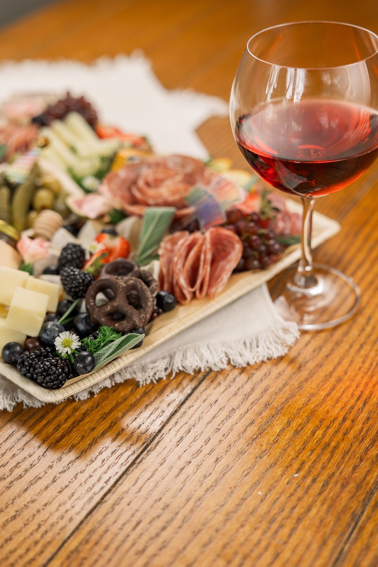 Elegant charcuterie board with cured meats, cheese, and olives paired with red wine on wooden table.
