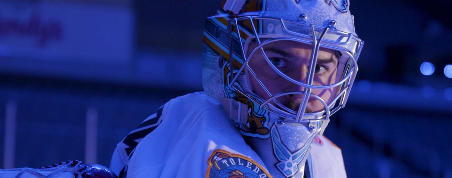 A hockey goalie in blue lighting on ice.