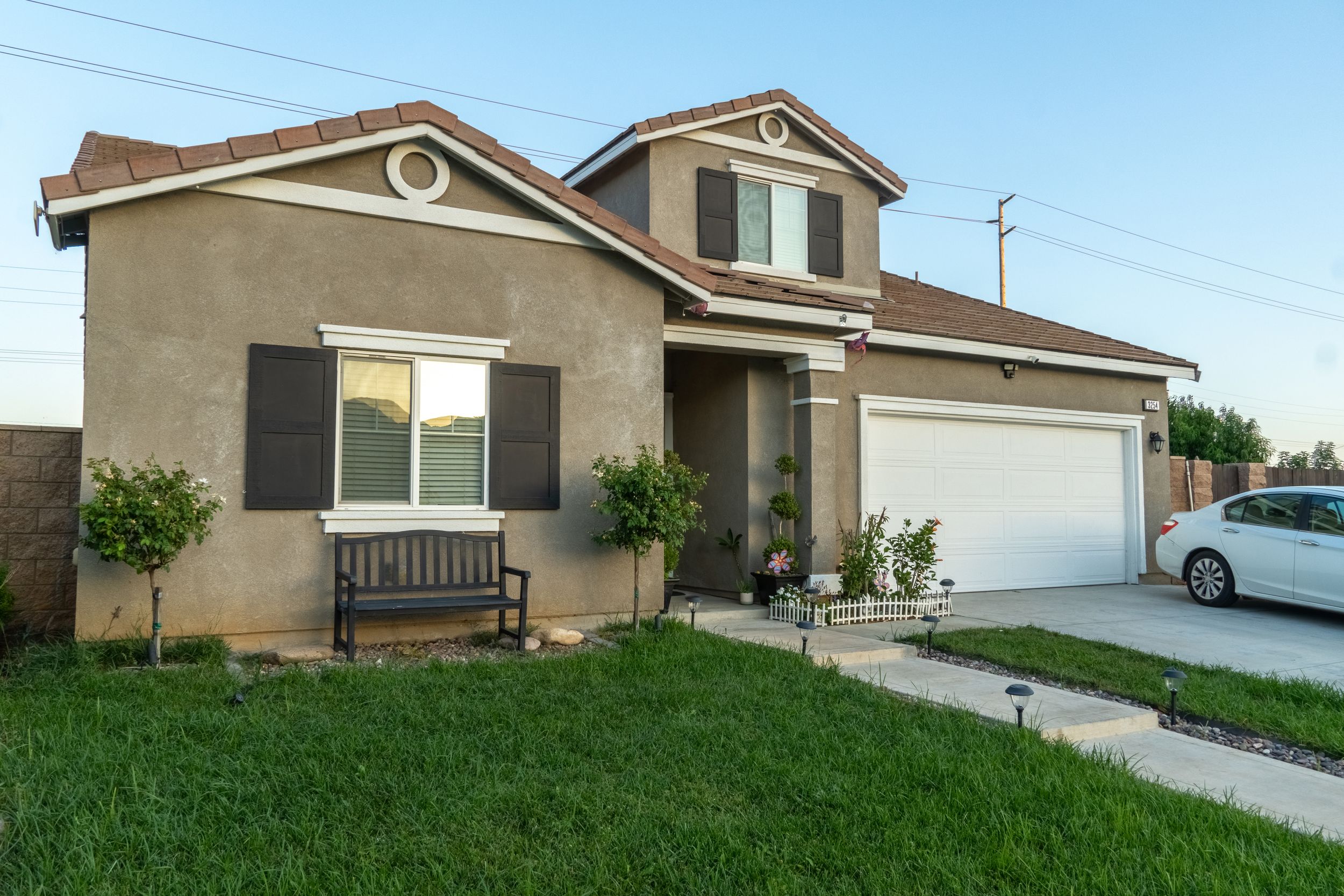 Two-story stucco home with attached garage, green lawn, and covered front porch with bench seating.