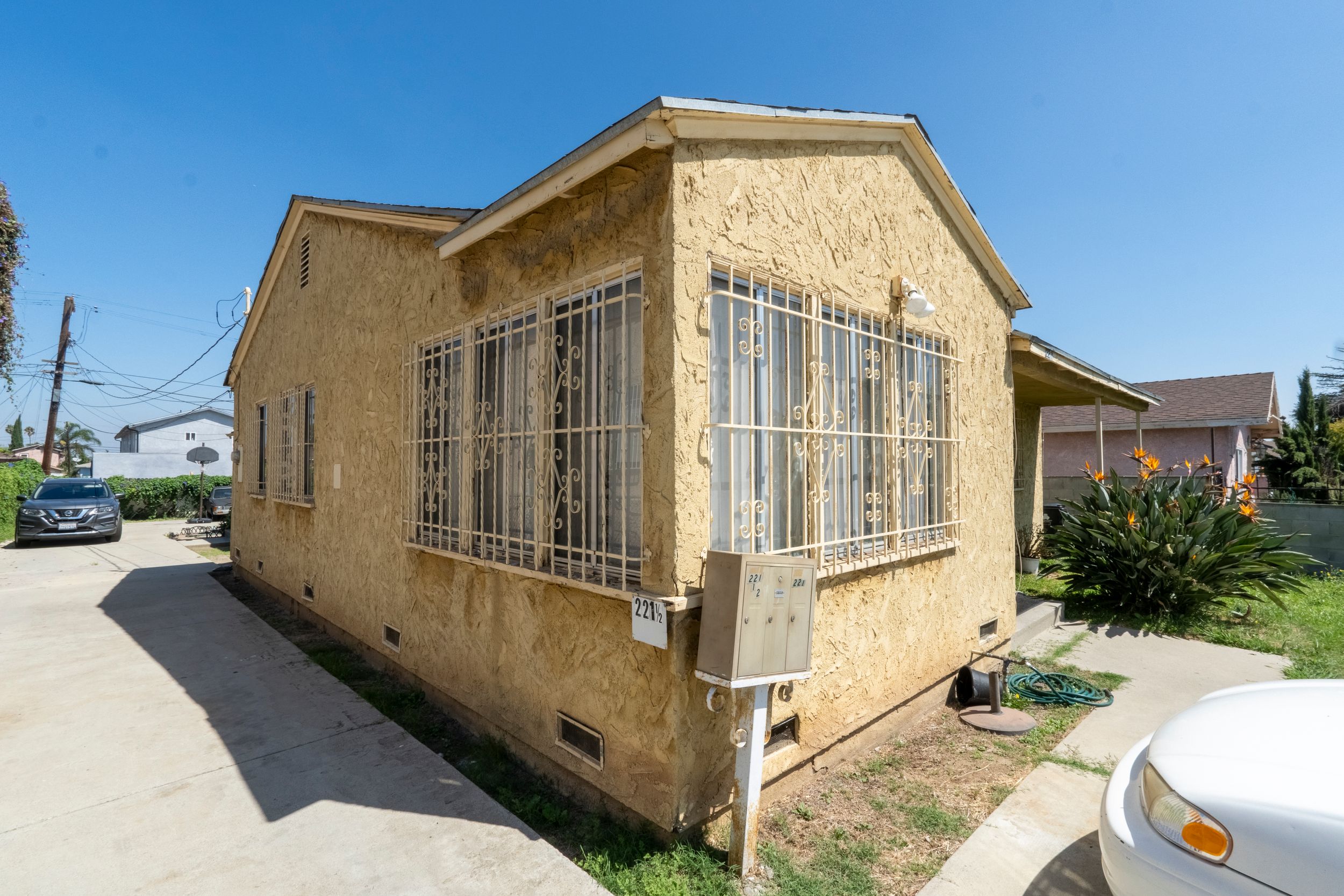 Small stucco home with barred windows and compact side yard in an urban residential neighborhood.