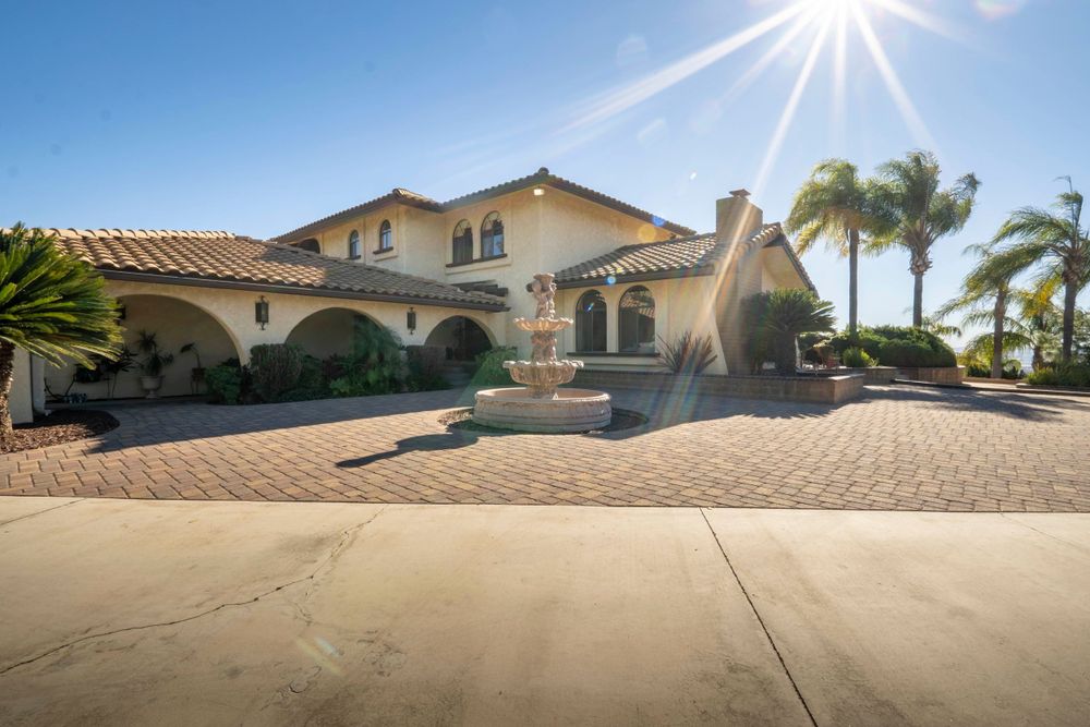 Grand Mediterranean-style estate with a fountain, palm trees, and brick paver driveway.