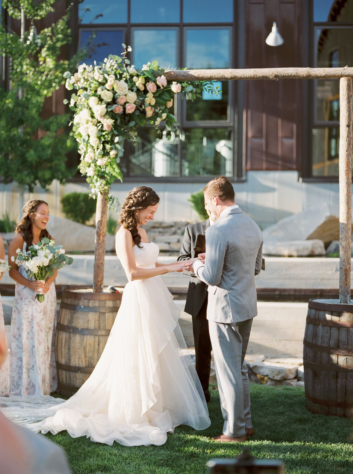Outdoor wedding ceremony under floral arch with rustic wine barrel decor.