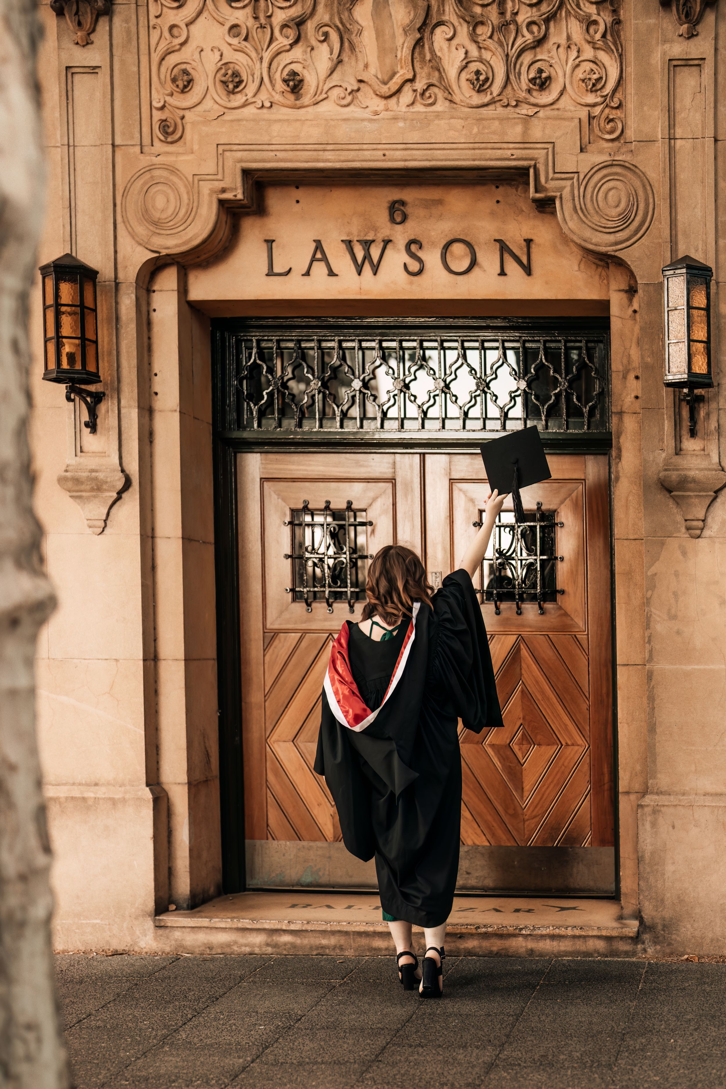 Graduate in cap and gown stands in front of ornate Lawson building entrance.
