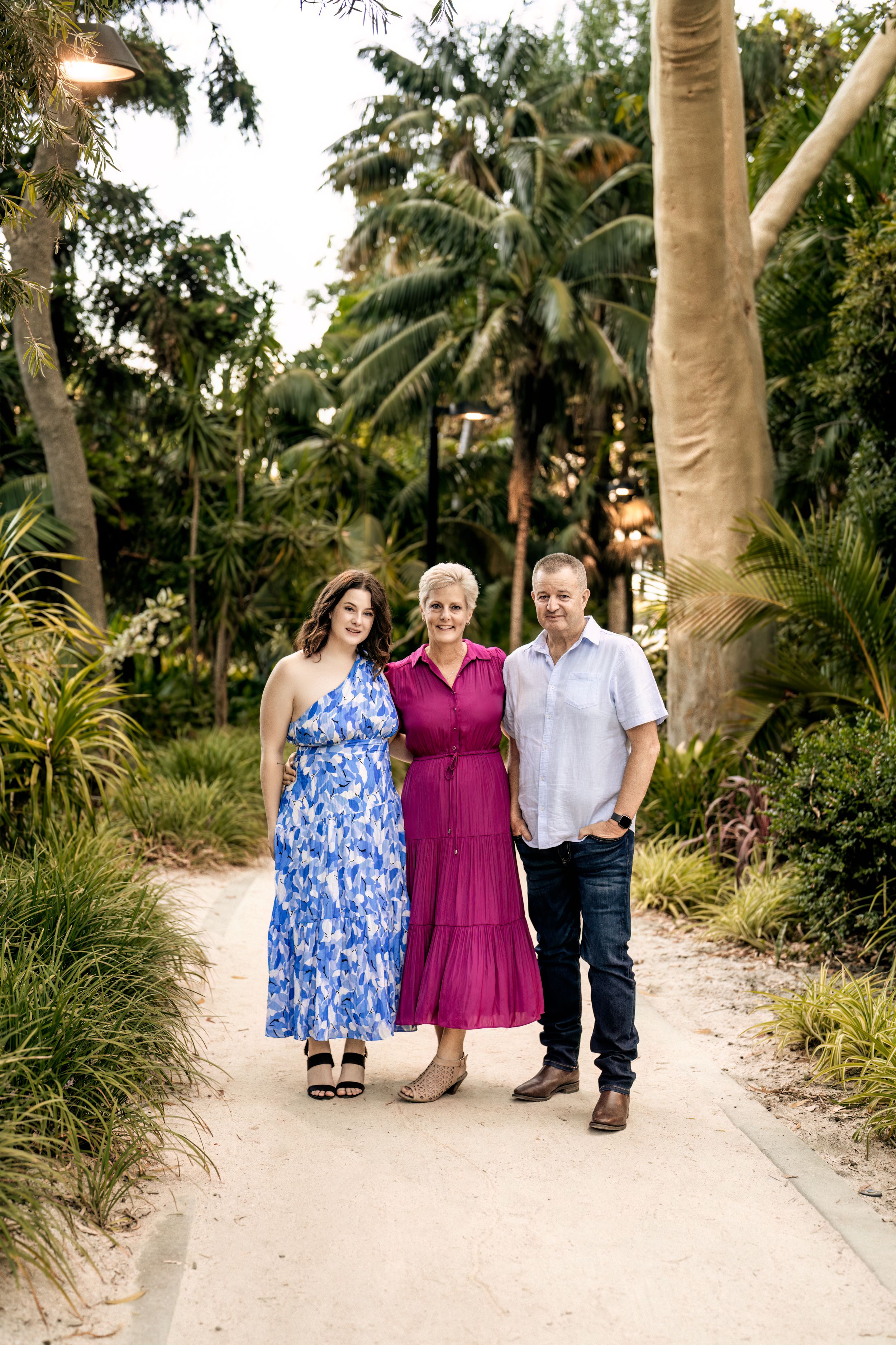 Three people walking together on a palm-tree lined path in casual attire.