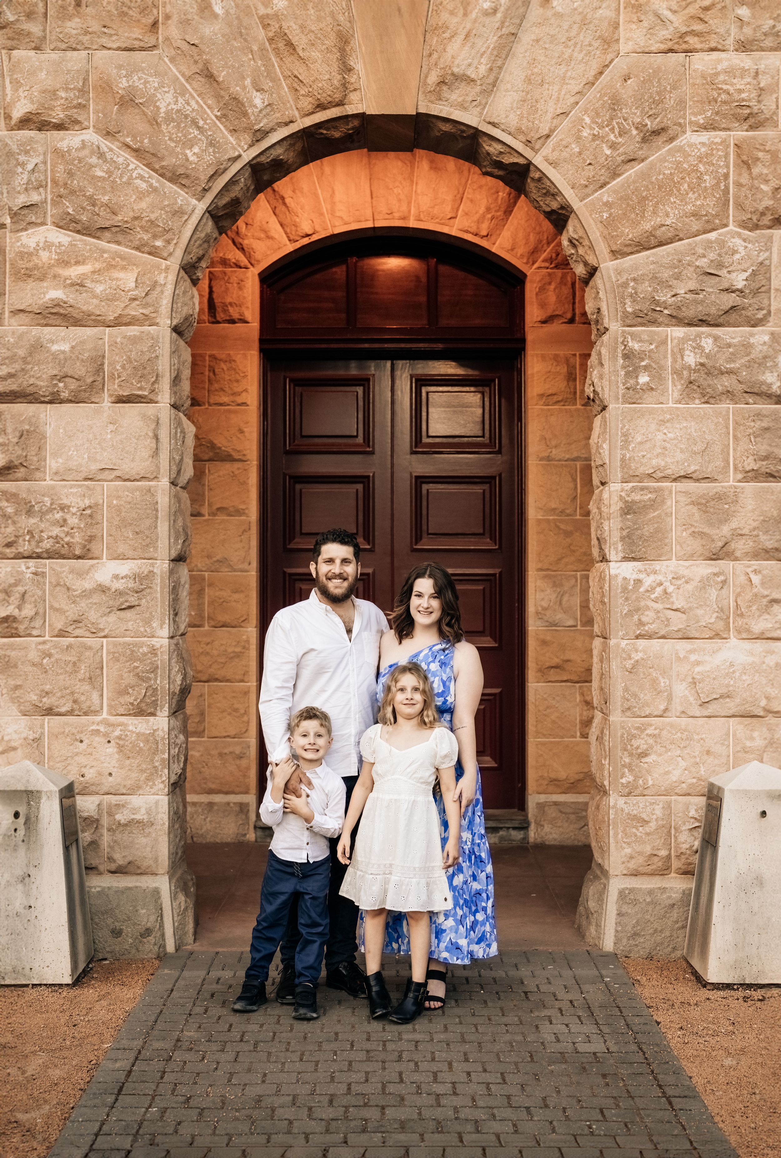 A family poses together in front of an ornate stone archway and wooden doors.