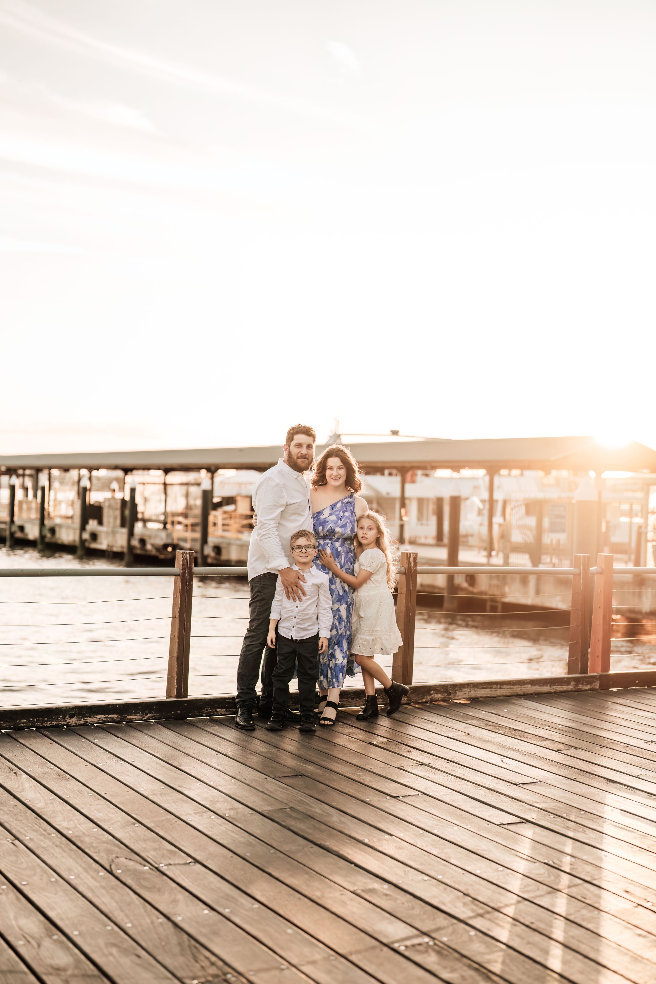 Family shares tender moments on wooden pier during golden hour.
