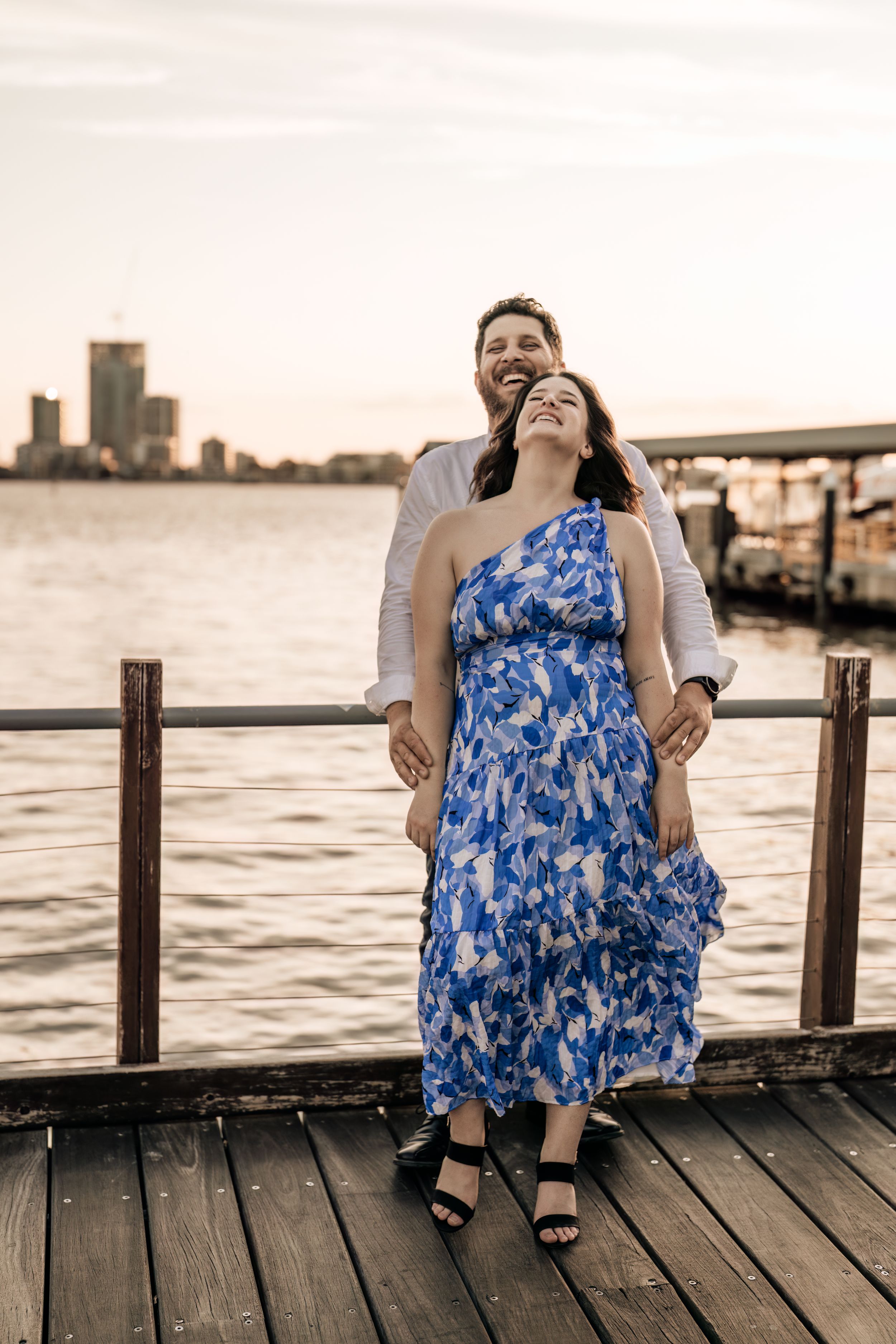 Couple shares playful moments on waterfront pier during sunset.