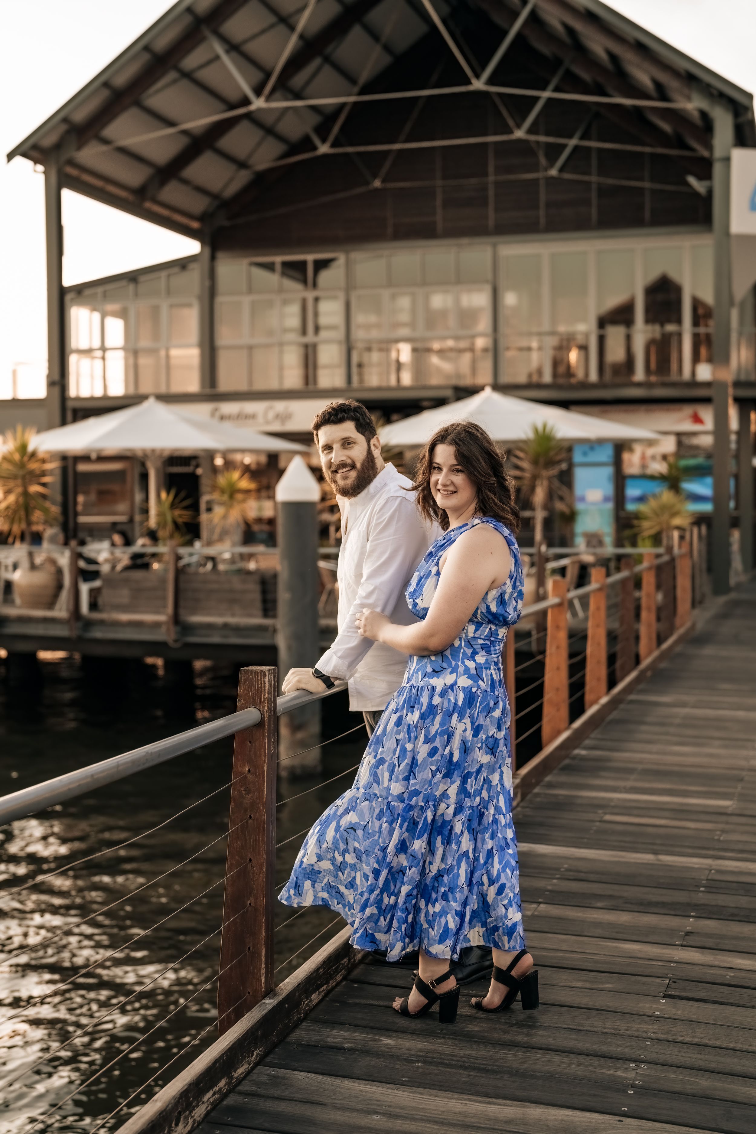 Couple poses romantically on wooden dock overlooking marina at sunset.