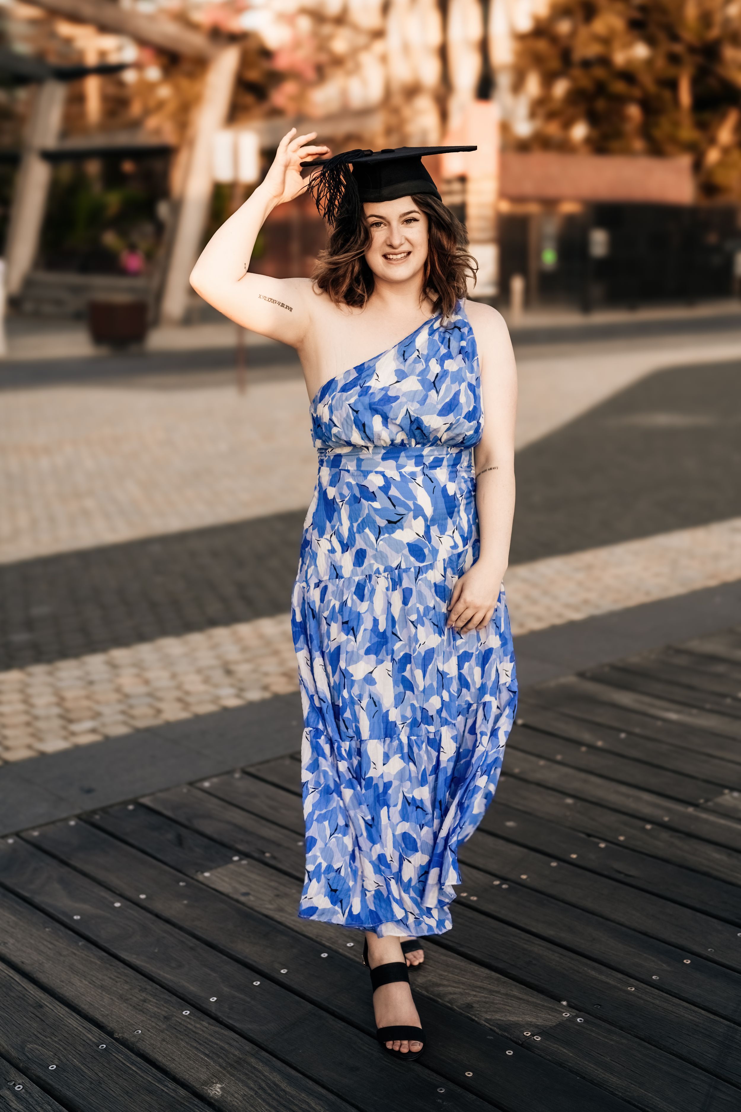 Woman in flowing blue dress poses playfully on wooden boardwalk.