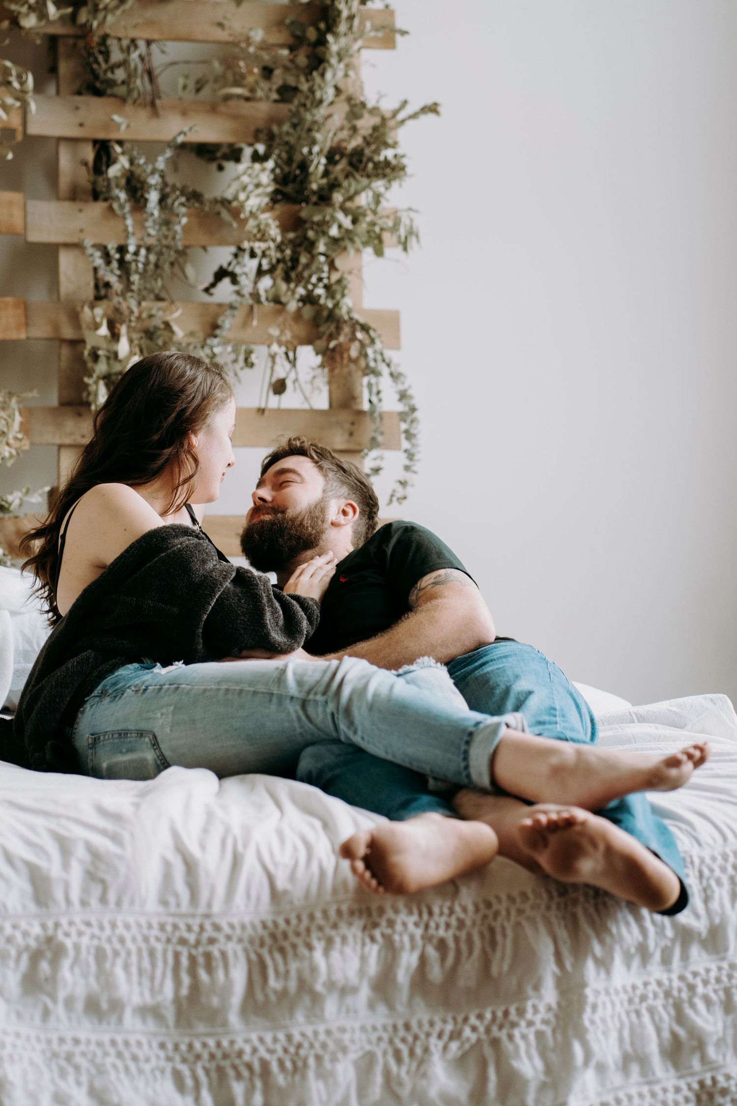 Relaxed maternity photo session on white bed with vine wall decor.