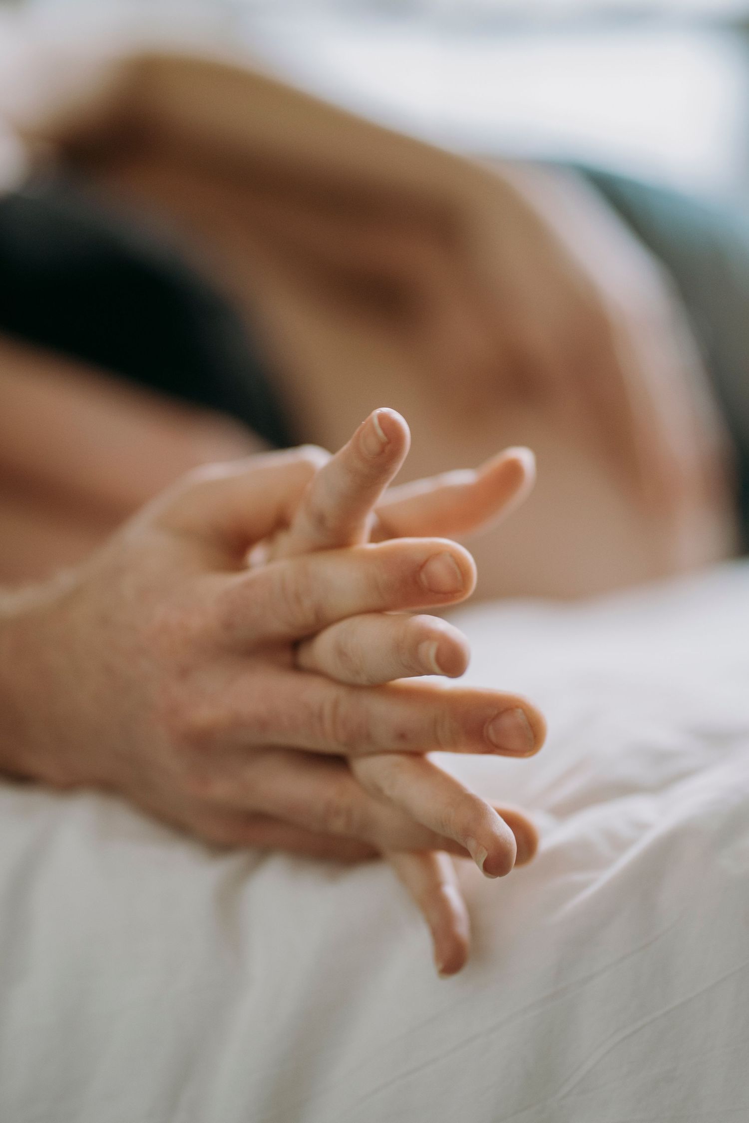 Artistic close-up of hands against white bedding in soft natural light.