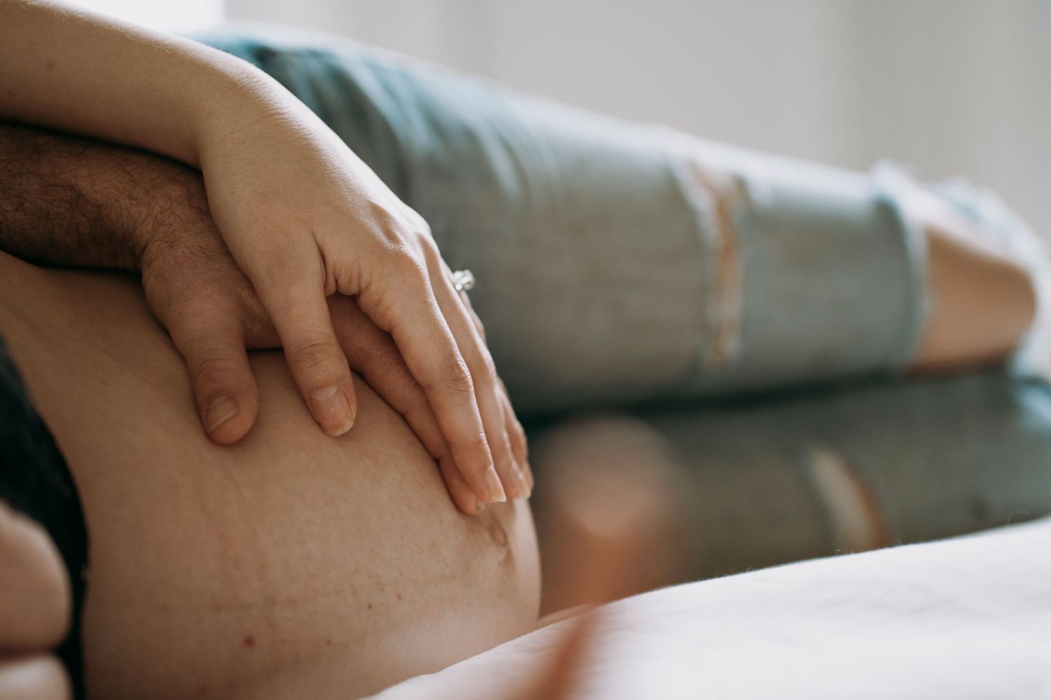 Hand gently resting on pregnant belly in intimate maternity photo.
