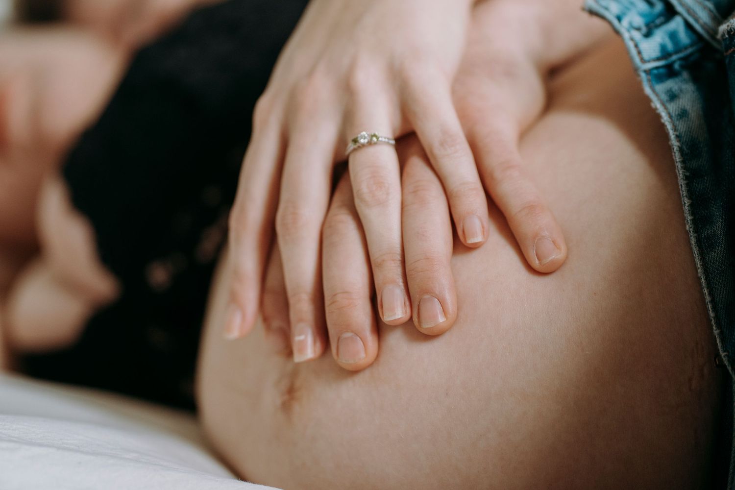 Close-up of hands with engagement ring resting on pregnant belly.