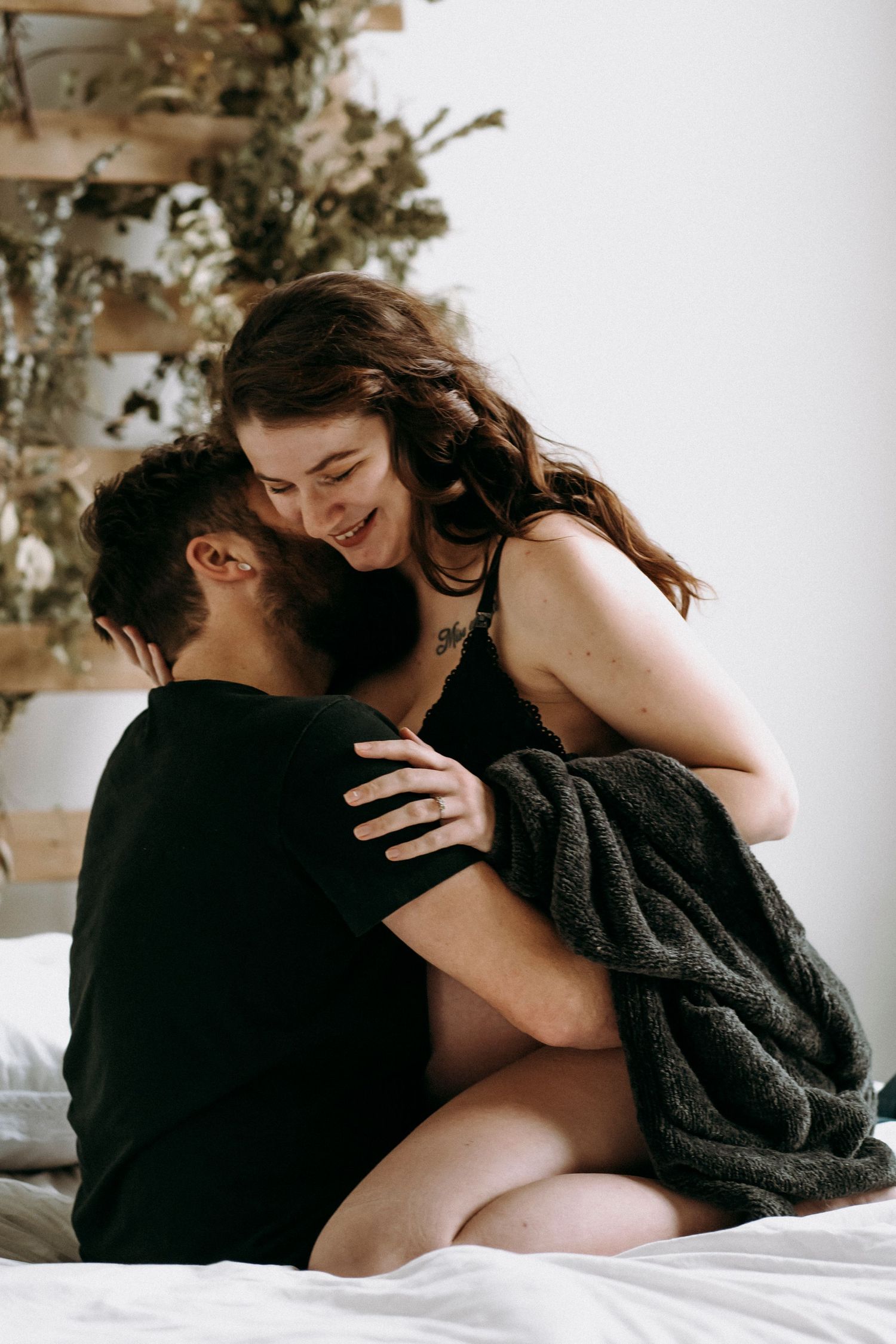 Couple embracing intimately on bed with decorative wall panel and greenery in background.