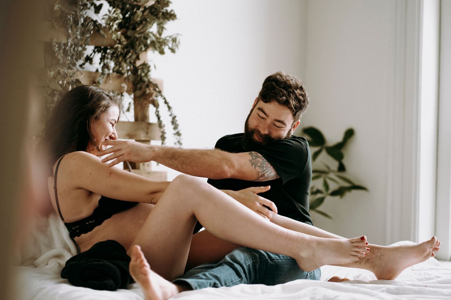 Couple relaxing together on white bedding against wooden wall with plants.