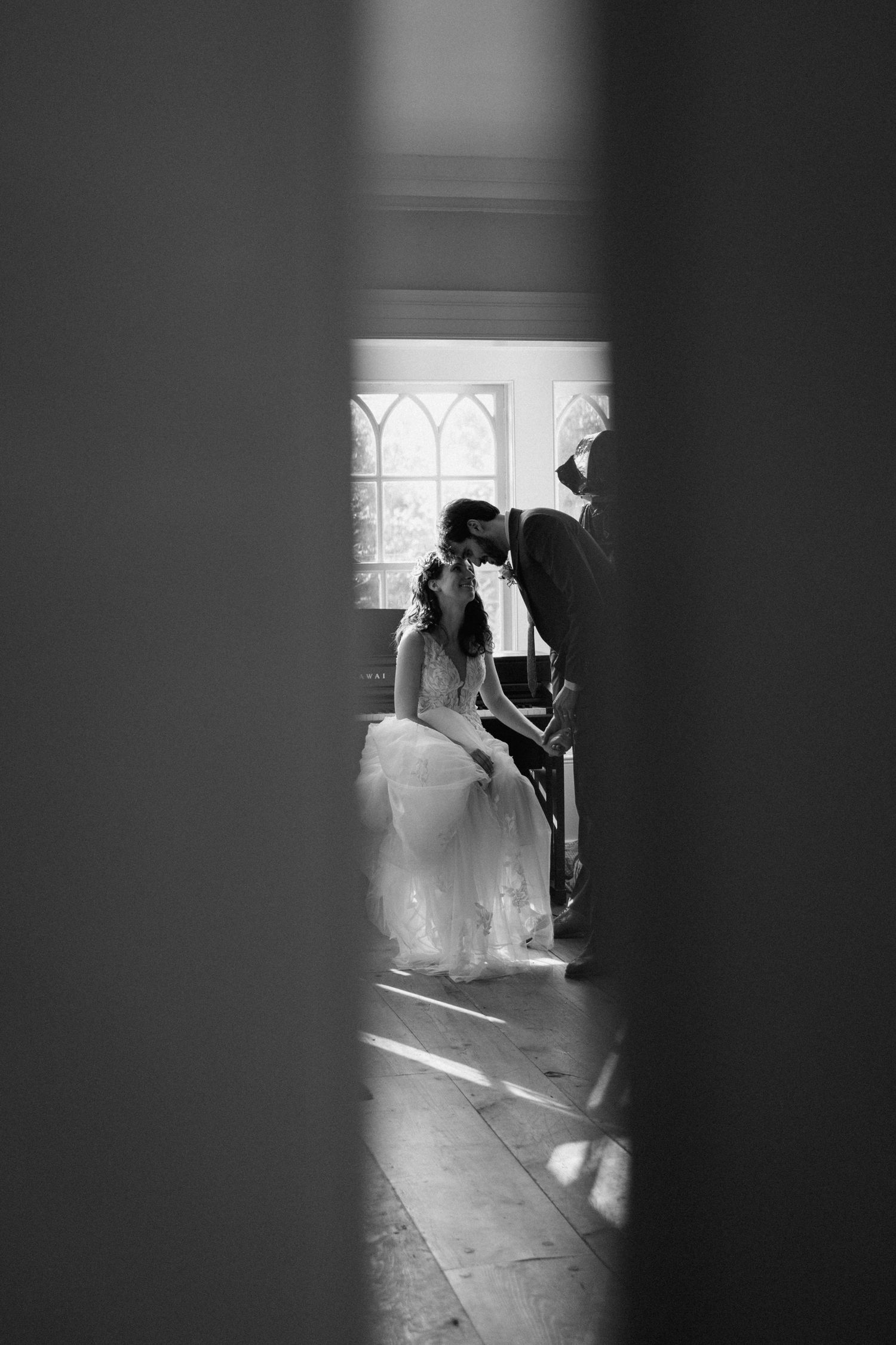 Black and white photo of wedding couple framed through doorway in church setting.