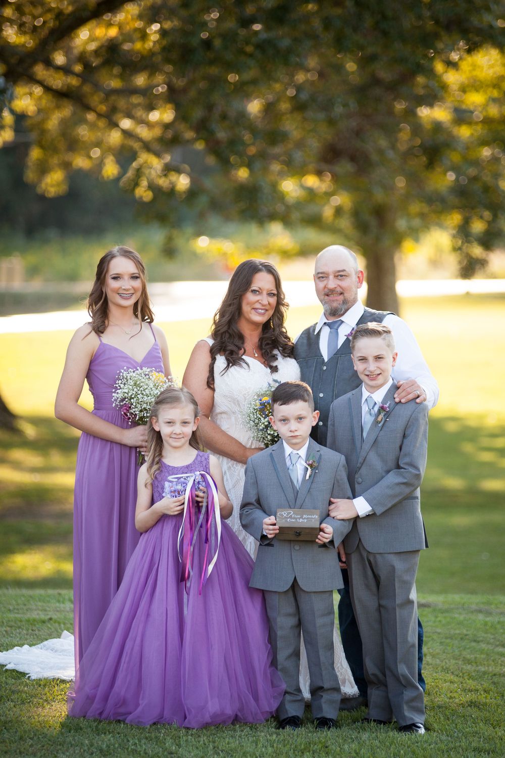 Wedding party poses together outdoors with purple bridesmaid dress and gray suits.