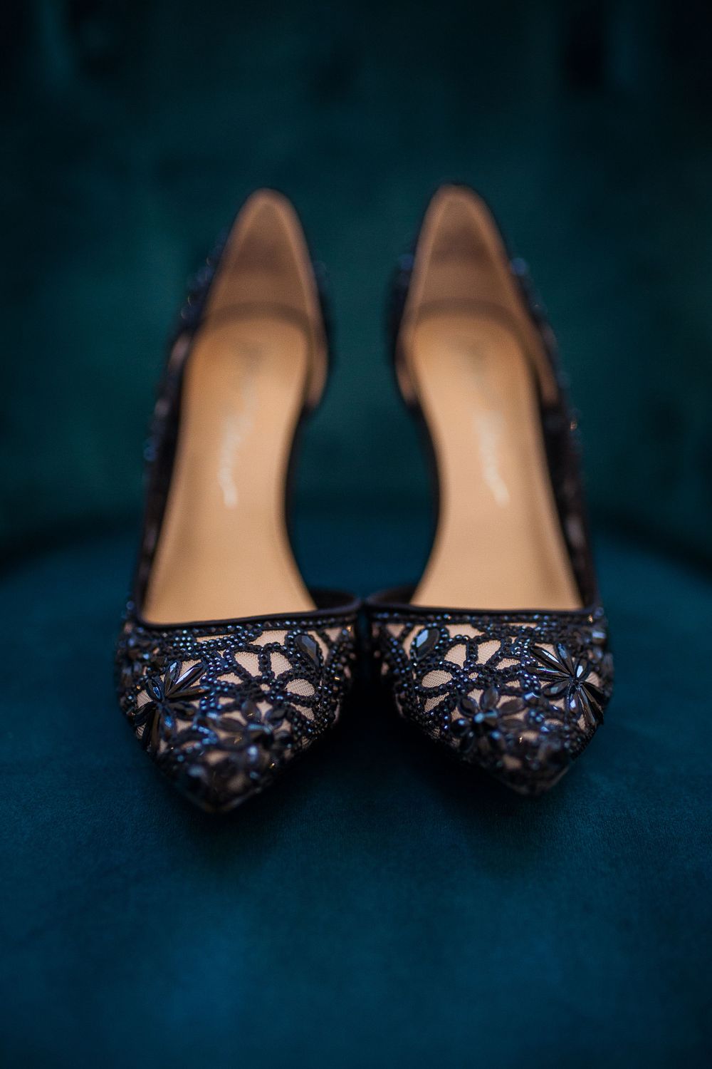 Elegant black lace floral pattern stiletto heels with pointed toes on a dark blue textured background.