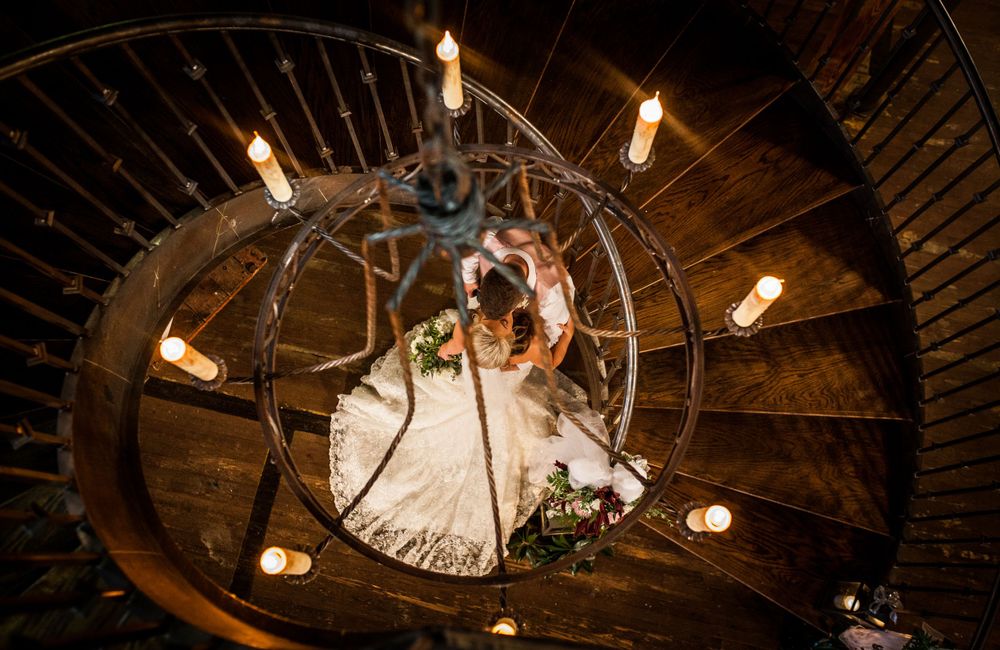Artistic overhead shot of bride on spiral staircase illuminated by vintage light fixtures.