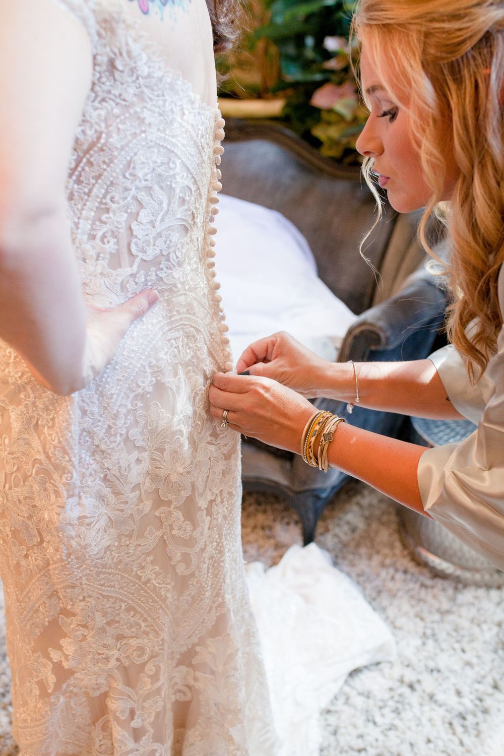 Close-up of intricate lace details being adjusted on a white wedding dress.