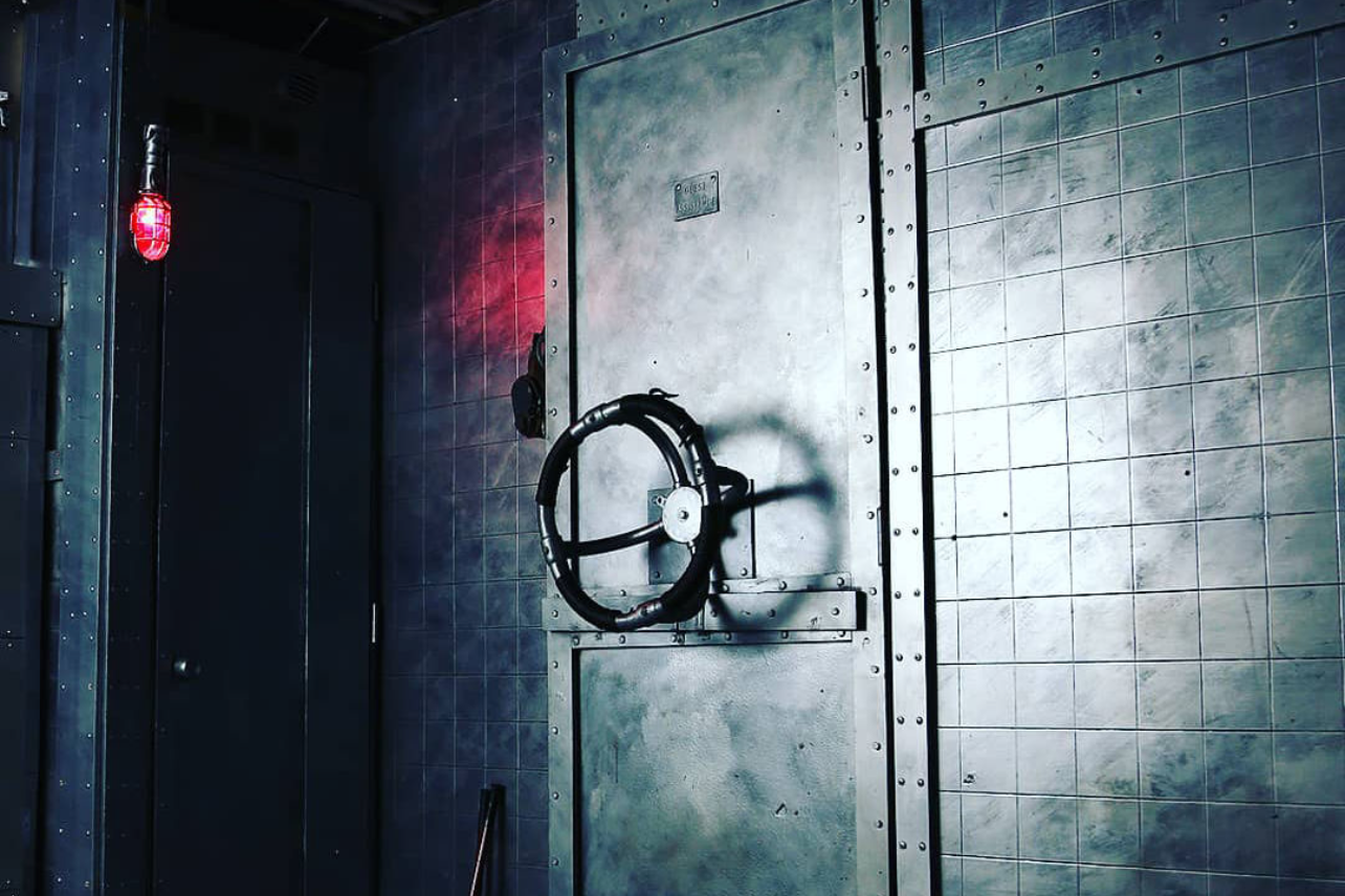 Dark industrial hallway with metal door and red emergency light casting eerie shadows.