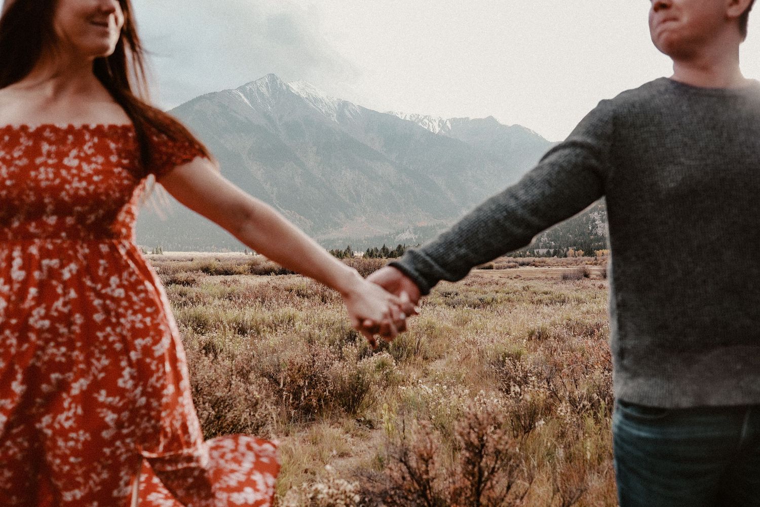 Couple holding hands in autumn landscape with mountains in background.