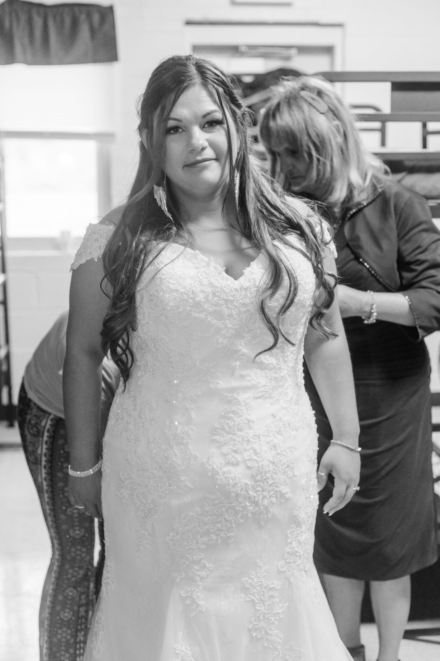 A bride in a white lace gown poses during wedding preparations.