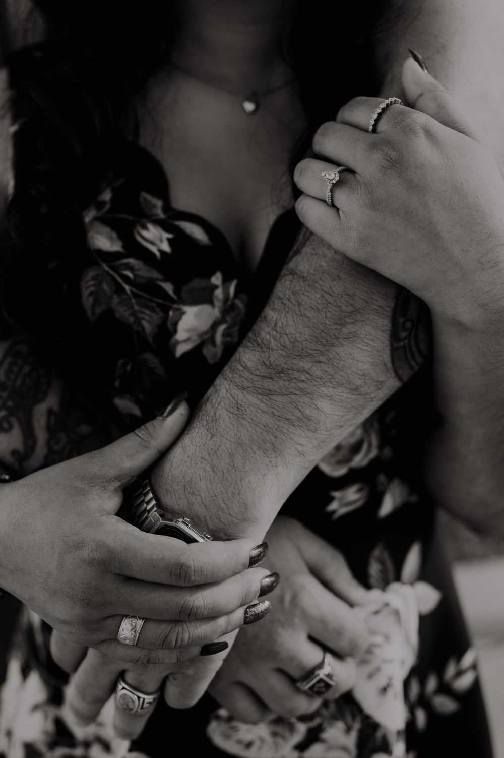 Black and white close-up of hands embracing against floral pattern.