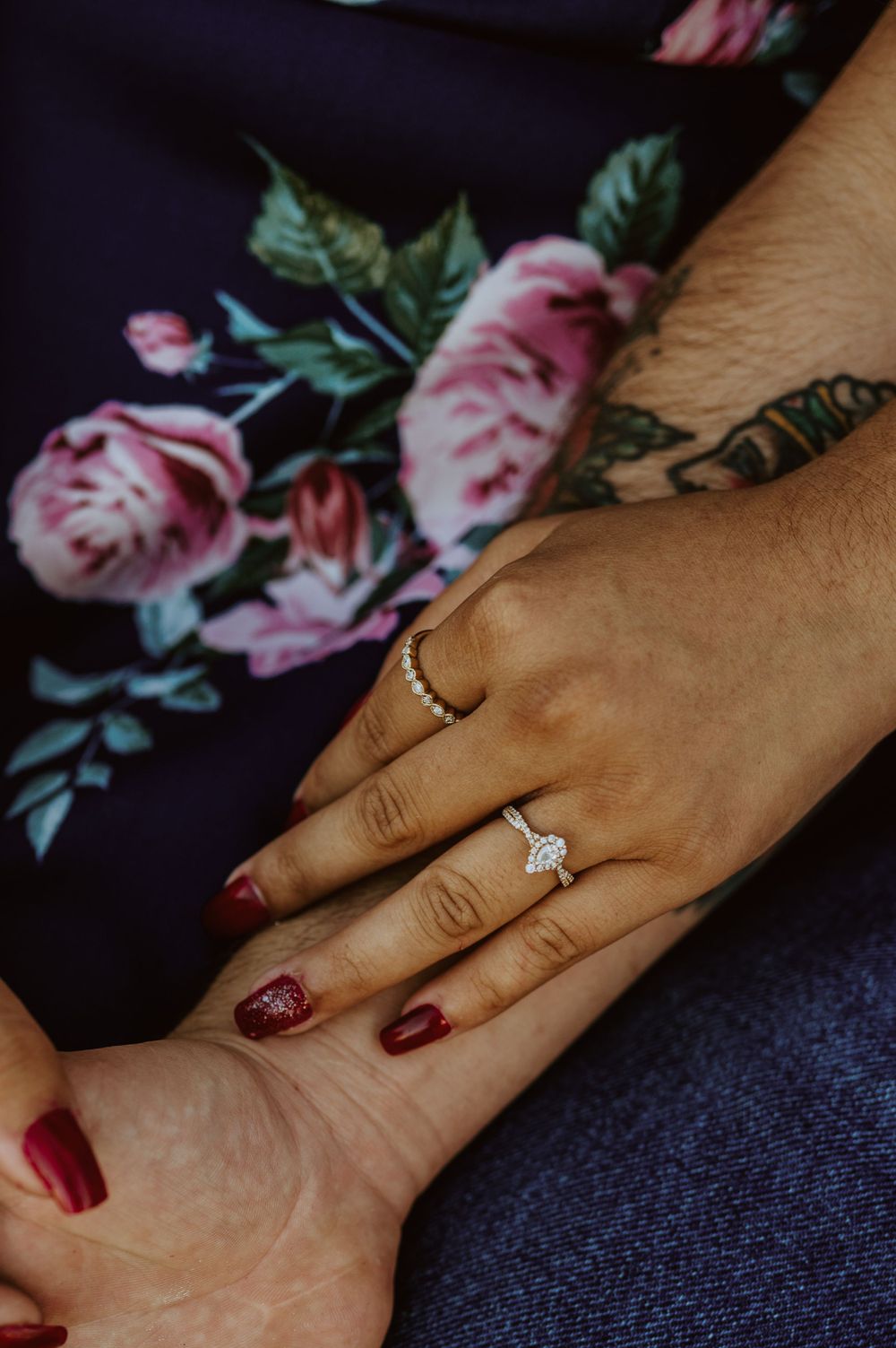 Close up of hands with red nail polish and engagement ring on floral fabric.
