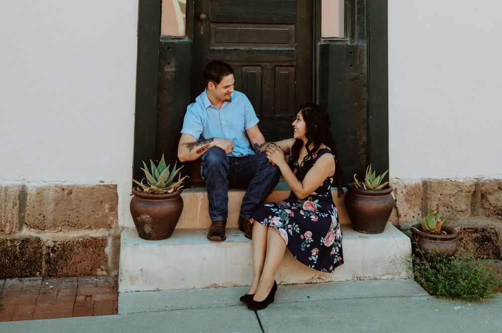 Couple sitting on steps by brown wooden door and clay planters.