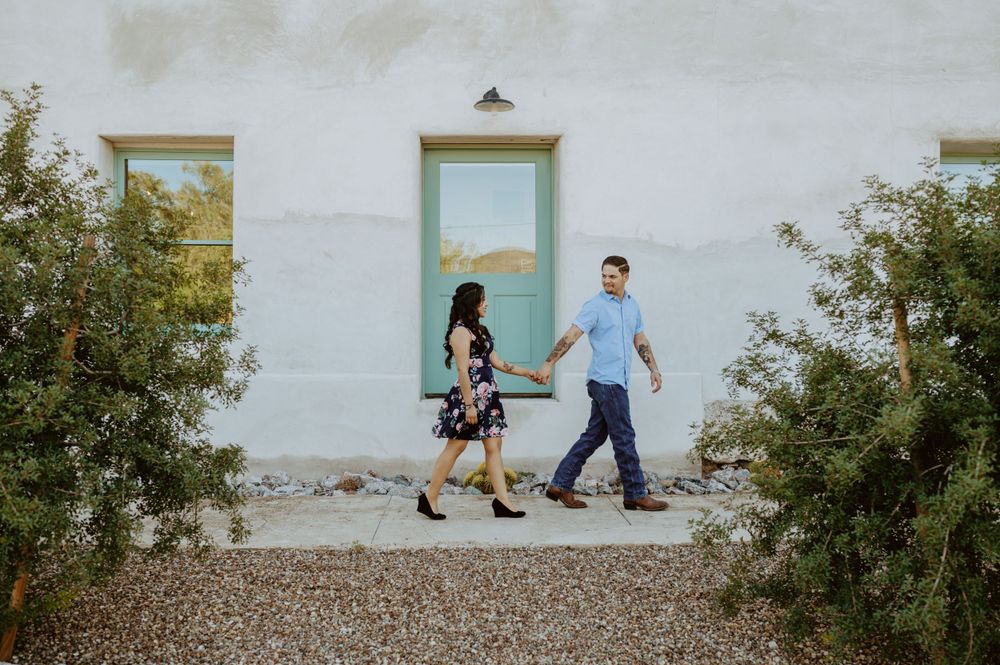 A couple sits together on stone steps against a white wall with a mint green door.