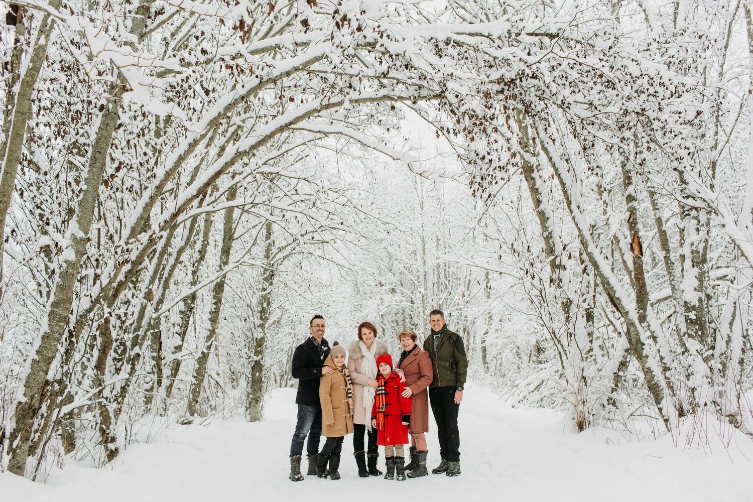 A family in winter gear posing in the snow, framed by snowy trees.