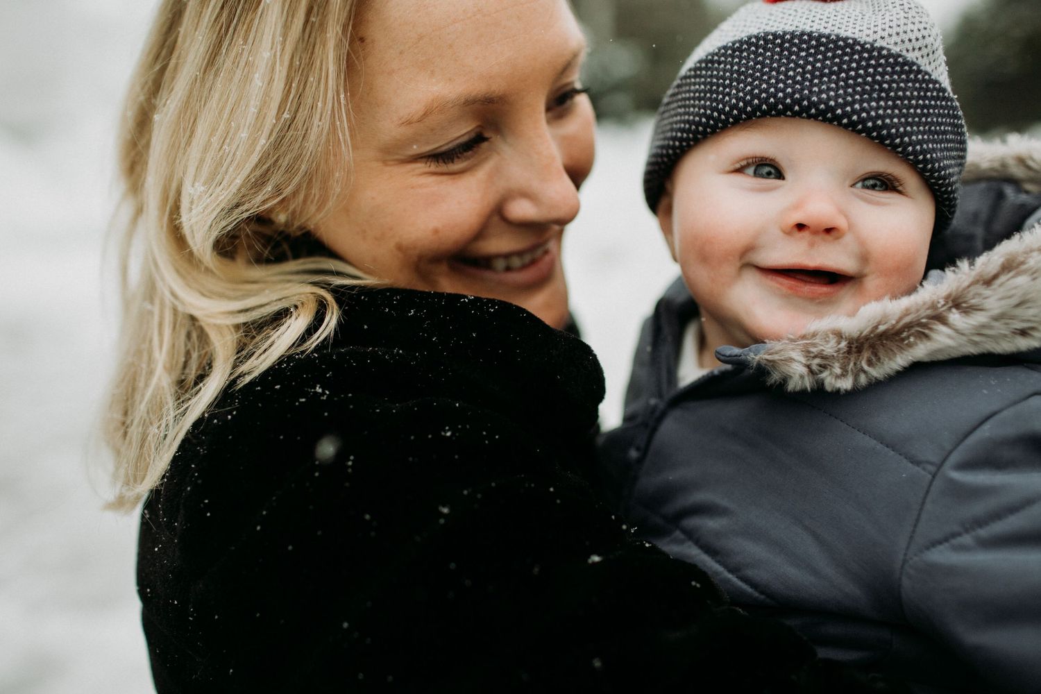 A parent and young child share a joyful moment together outdoors in winter clothing.