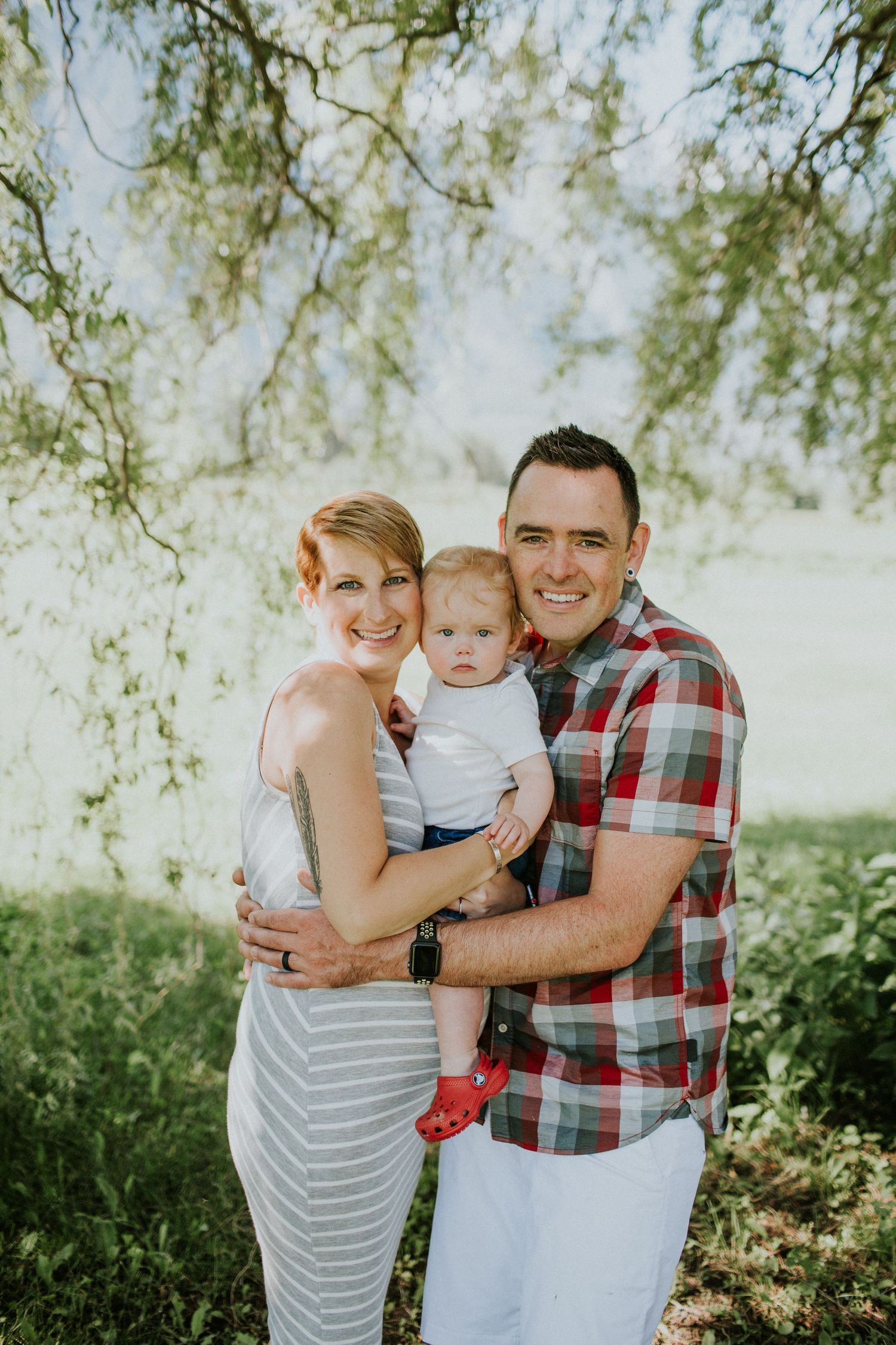 Couple holding baby daughter together under a tree in the summer.