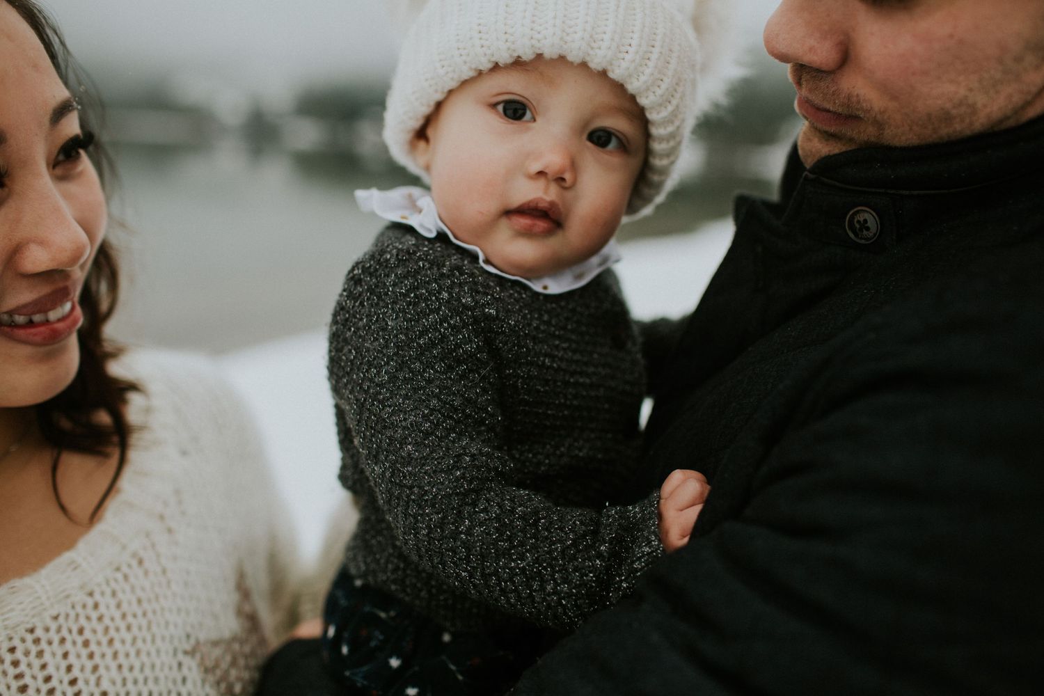 A couple and small child with a white toque on in snowy Whistler.