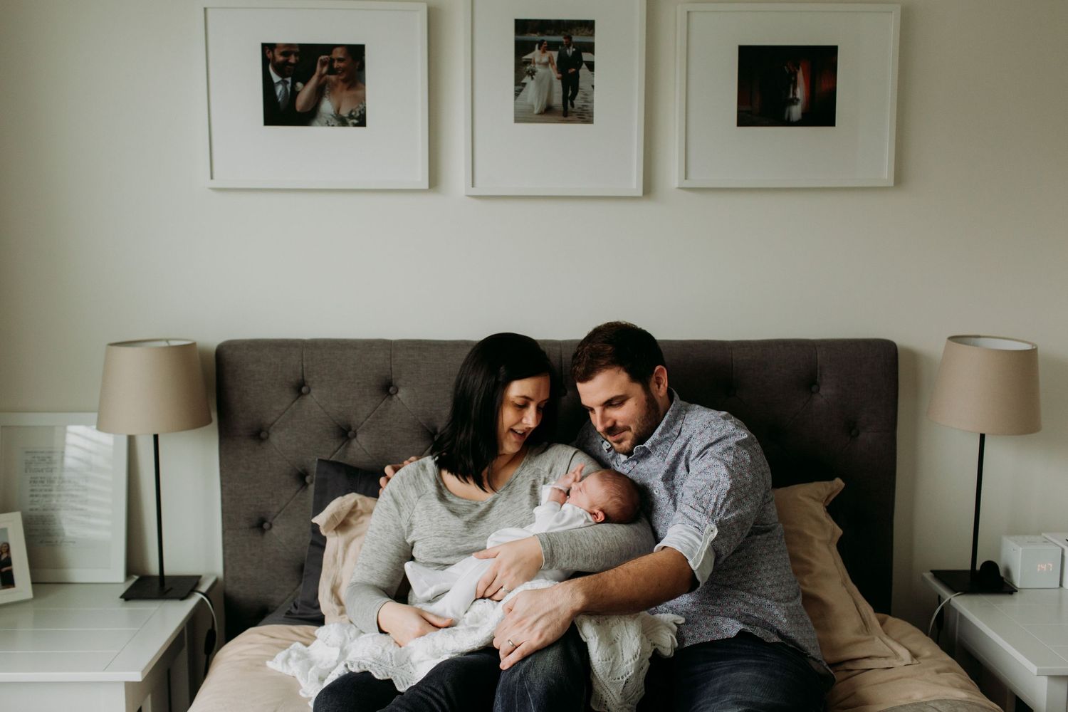 A new mom an dad hold their newborn baby on the couch together.