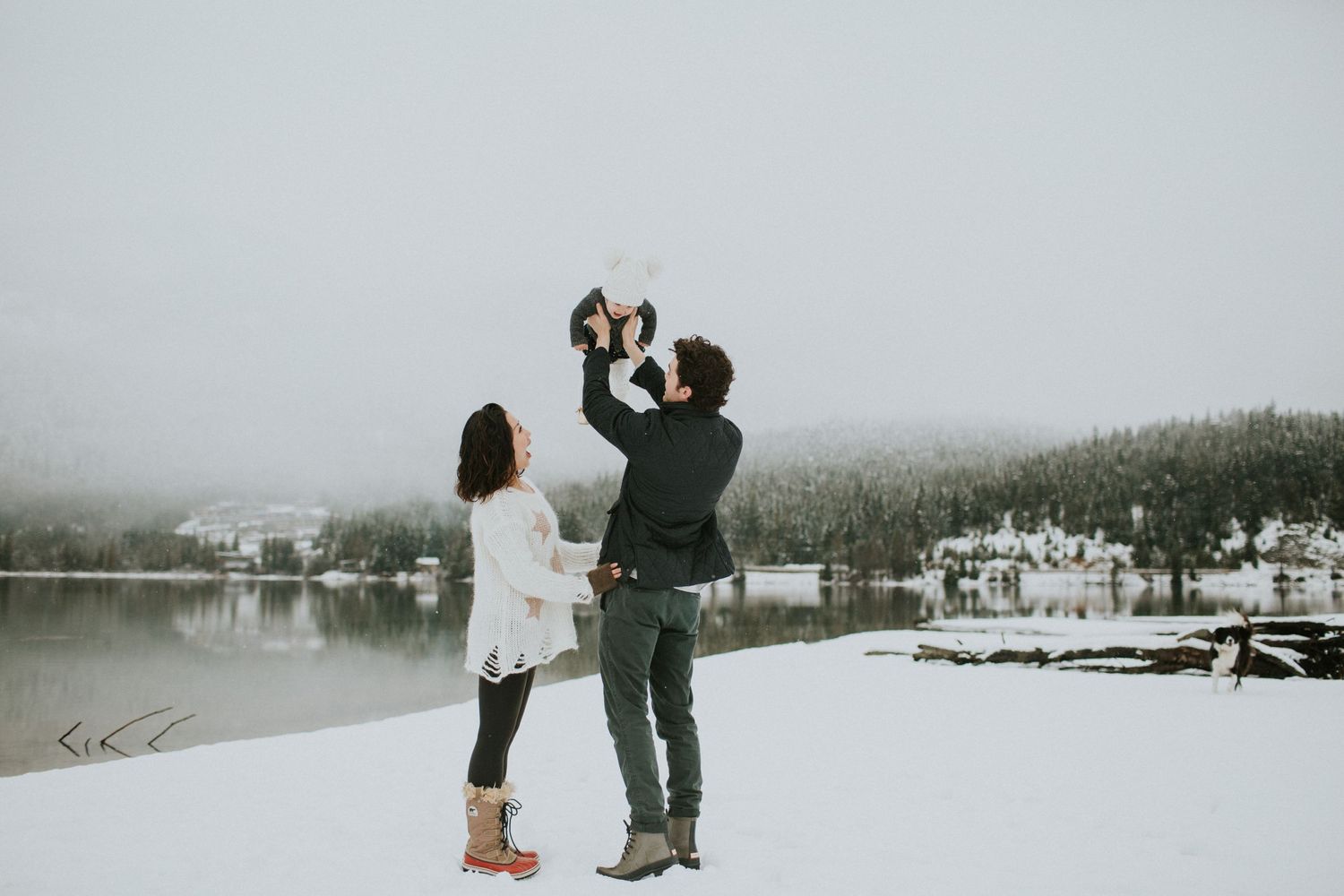 Dad holds up baby in the air with mom by his side.