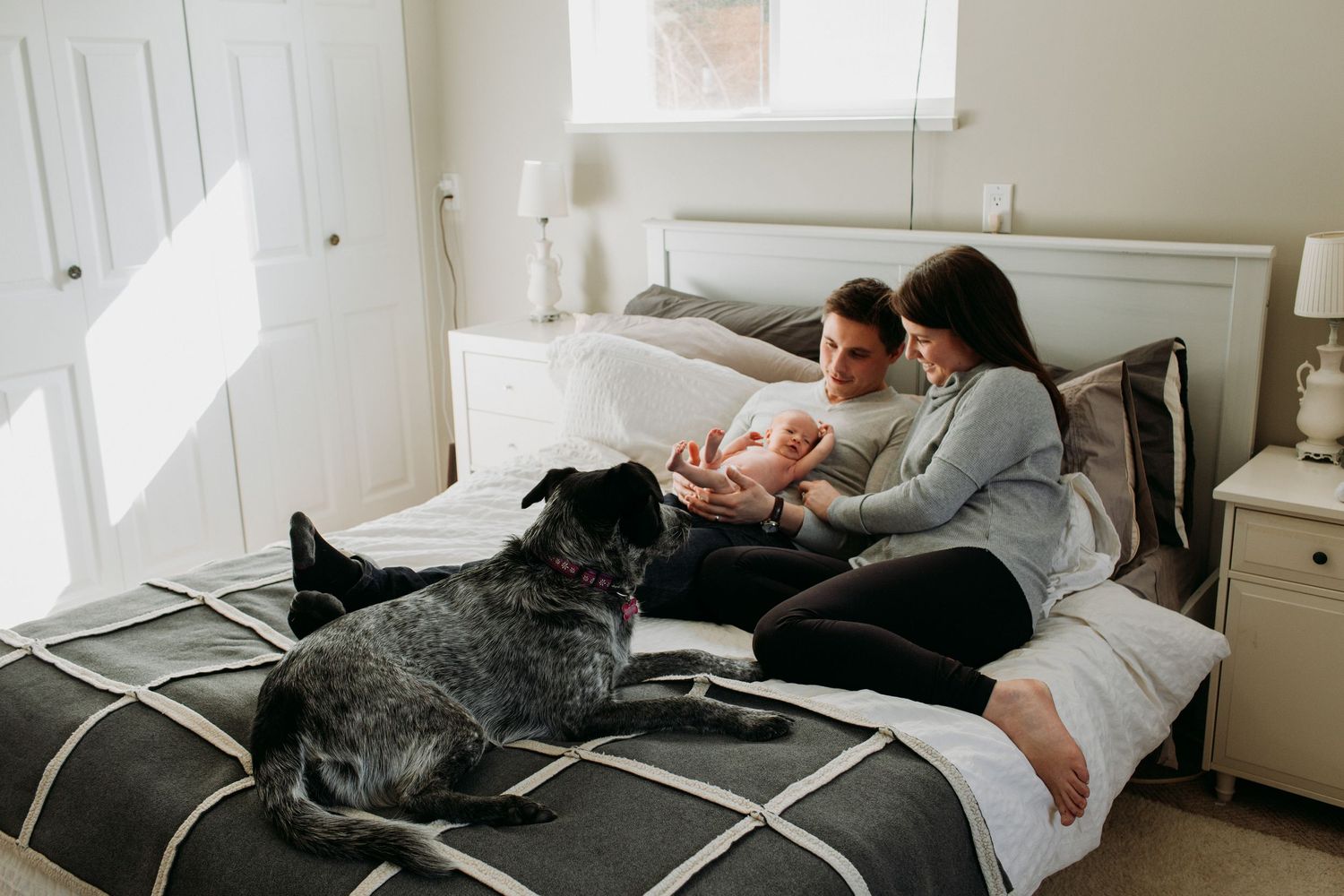 Couple with newborn and dog on bed.