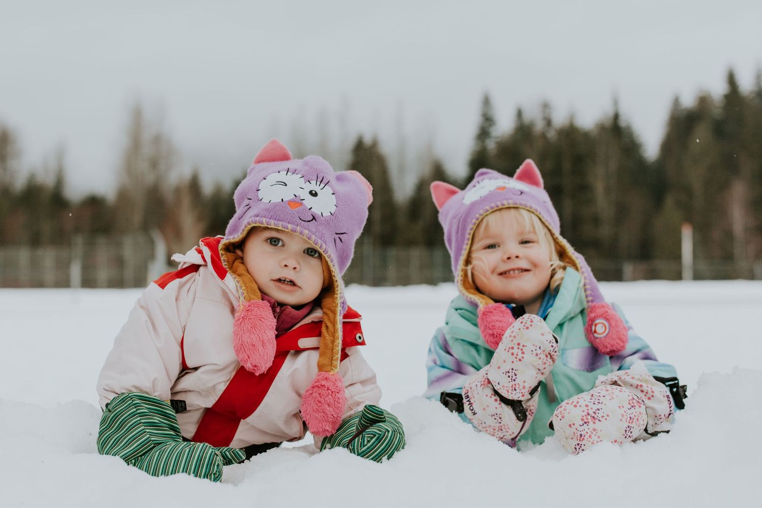 Two young sisters in full snow suits and beanies in the snow.