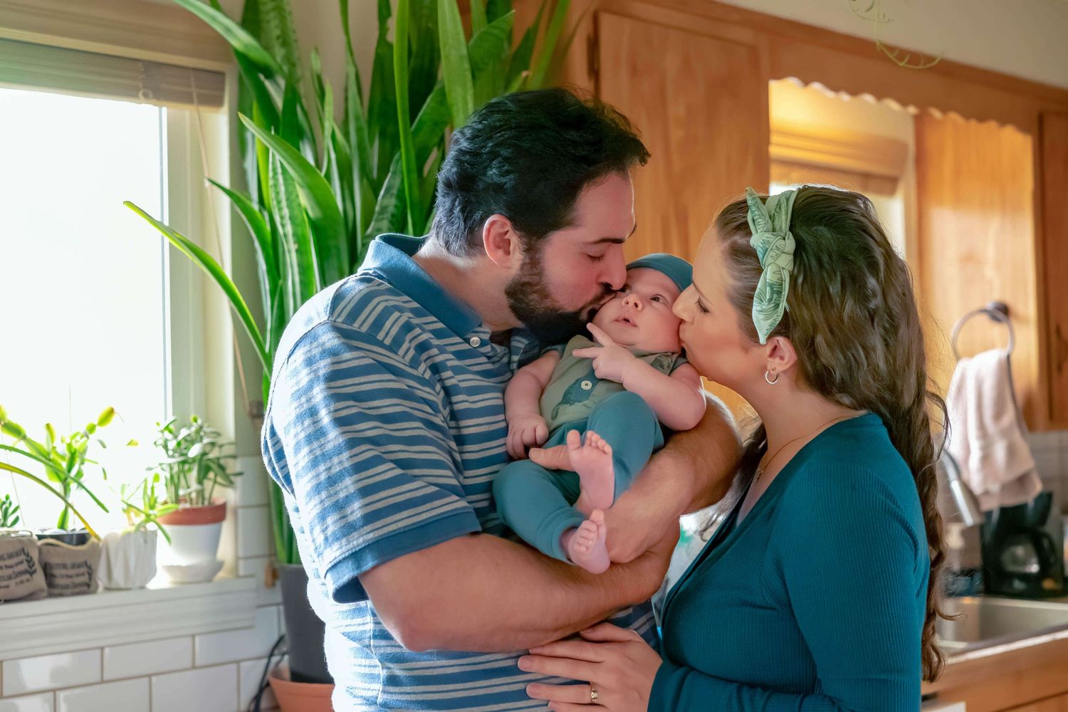dad and mom kiss baby boy on the cheek in the kitchen
