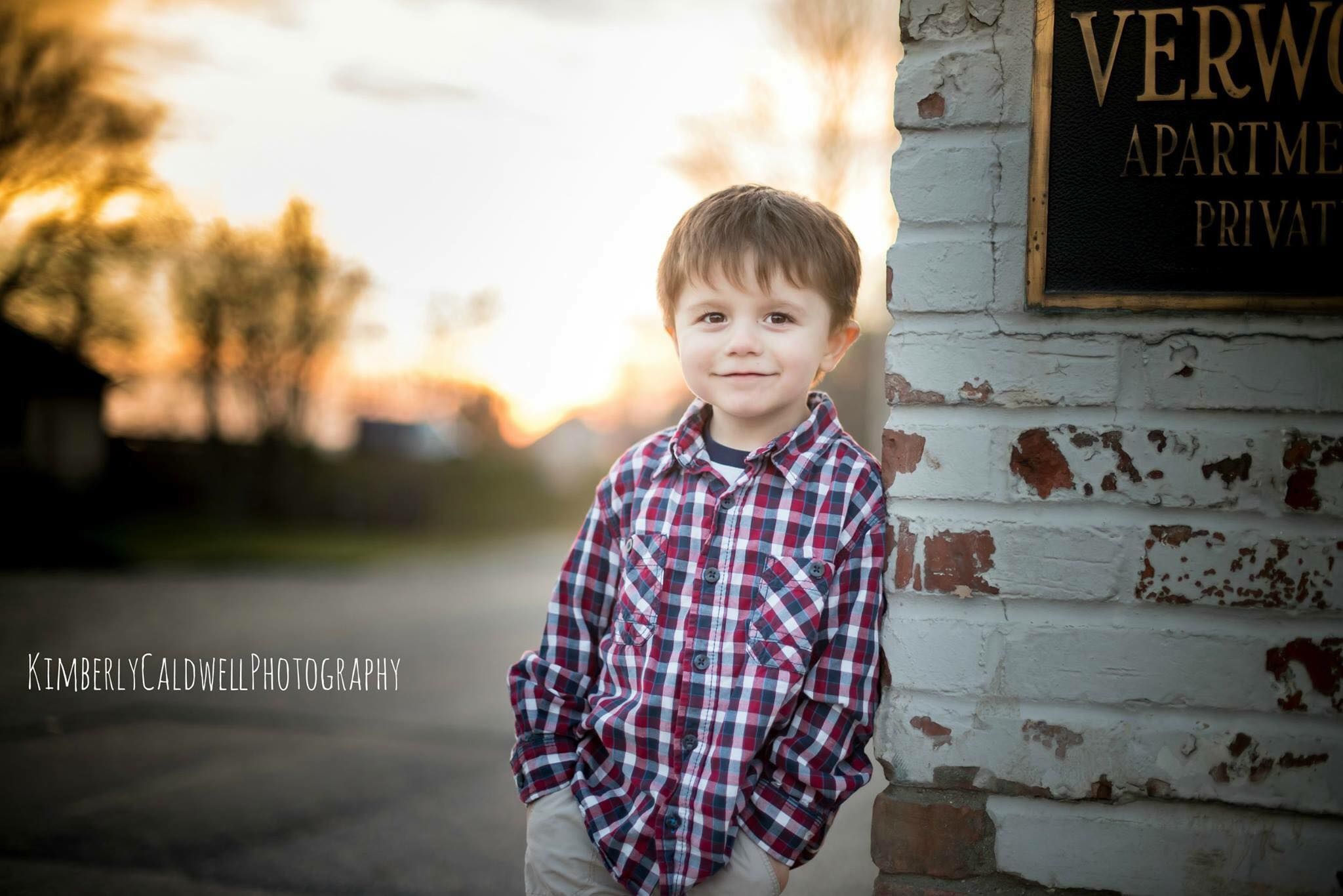 A sunset portrait of a young child in plaid shirt against a weathered white wall.