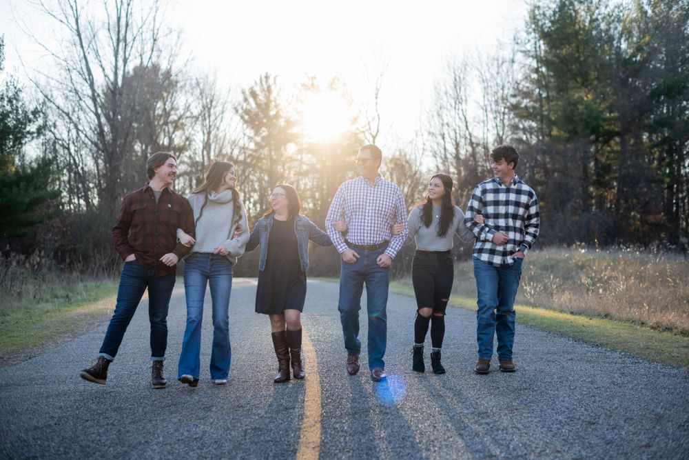 A group of six people stand together on a country road at sunset.