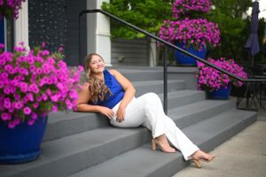 Person in white dress reclines on steps with vibrant purple flowers in planters.